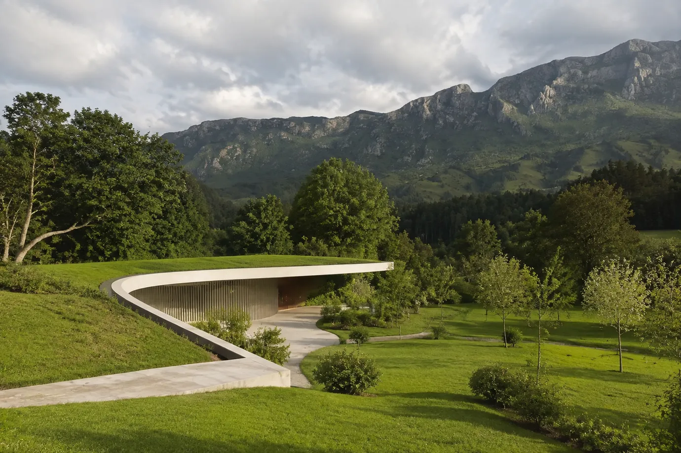 giantA earth-sheltered green home built into a landscaped hillside — curved glass facade, timber screening and living roof integrated with native Australian terrain